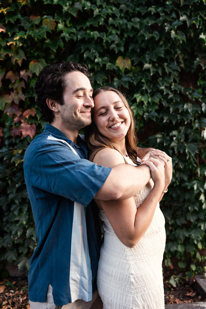 Happy couple embraces in front of a leafy green wall during their Roscoe Village engagement session