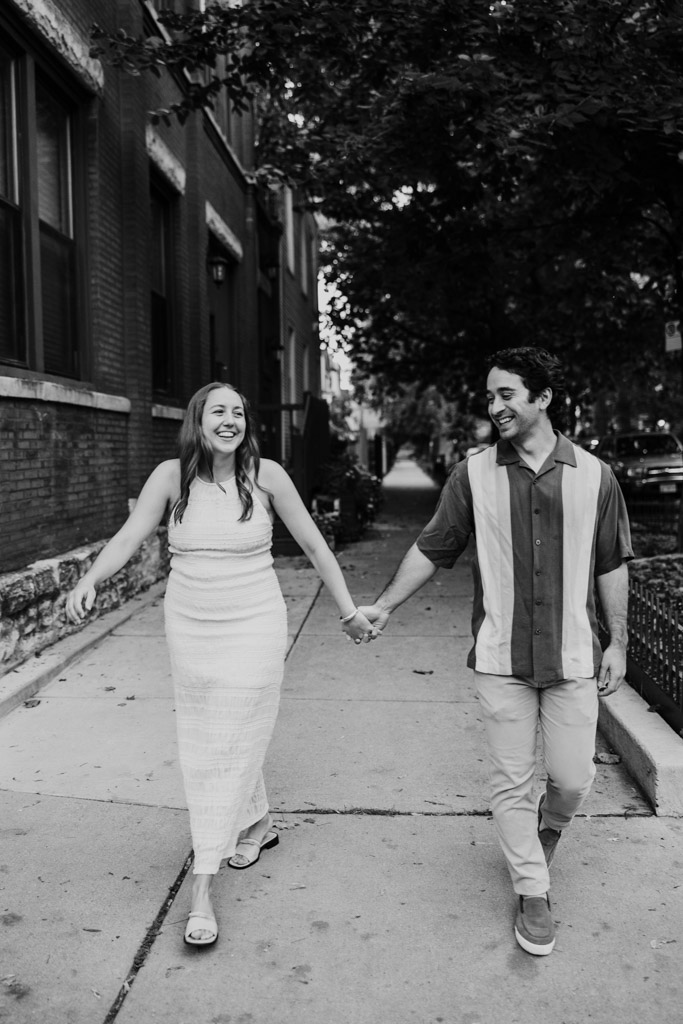 Black and white photo of engaged couple holding hands while walking down a Roscoe Village sidewalk