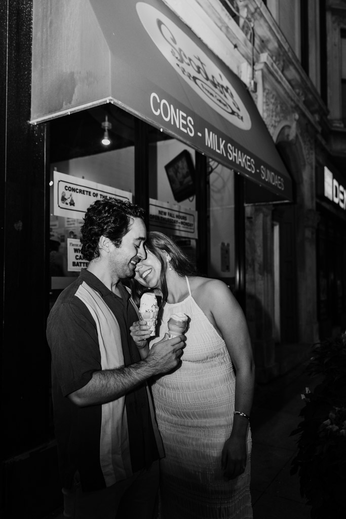Black and white photo of happy couple eating ice cream cones outside Scooters Frozen Custard at night during Roscoe Village engagement session