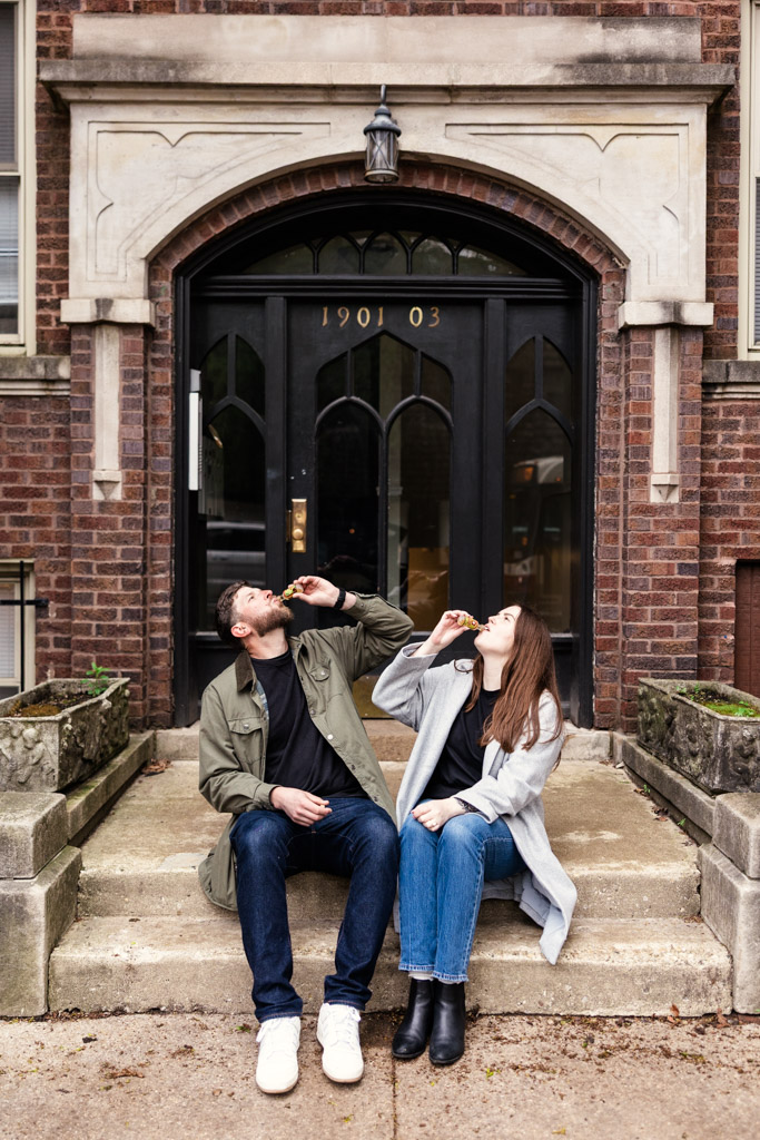 A man and woman sit on steps outside a doorway, both looking up and drinking from small bottles, sharing a quiet sunrise engagement.