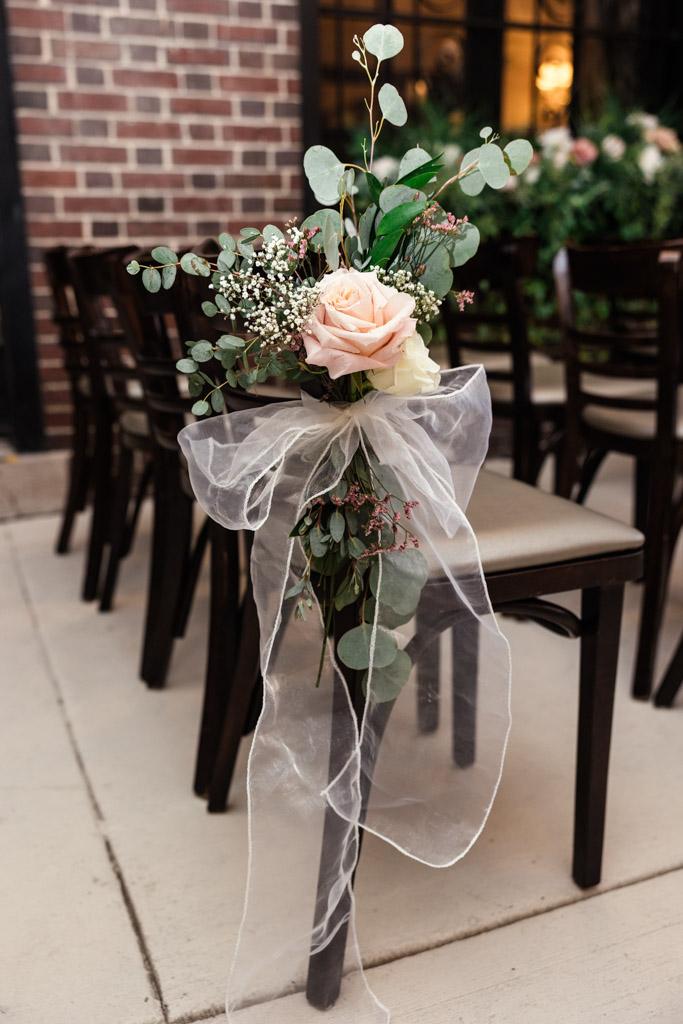 A pink rose and greenery bouquet tied to a chair with sheer white ribbon for wedding ceremony at Salvatore's in Chicago