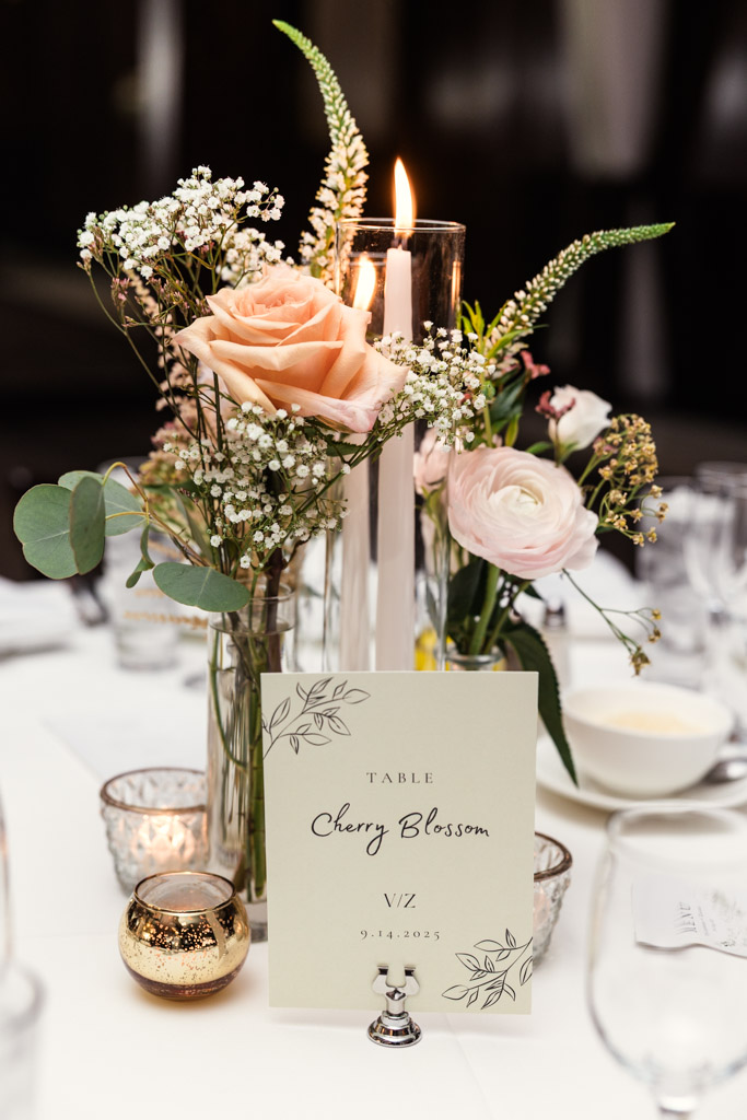 Floral centerpiece with candles, roses, and table card on a white tablecloth at Salvatore's wedding reception
