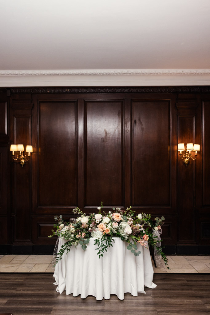 Round sweetheart table with a white cloth and a floral arrangement sits in front of a dark wood paneled wall for wedding reception at Salvatore's