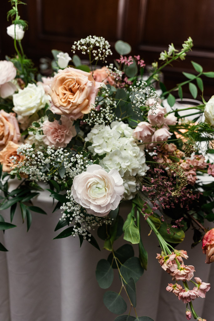 A floral arrangement with white, peach, and pink roses, hydrangeas, and greenery on a table at Salvatore's