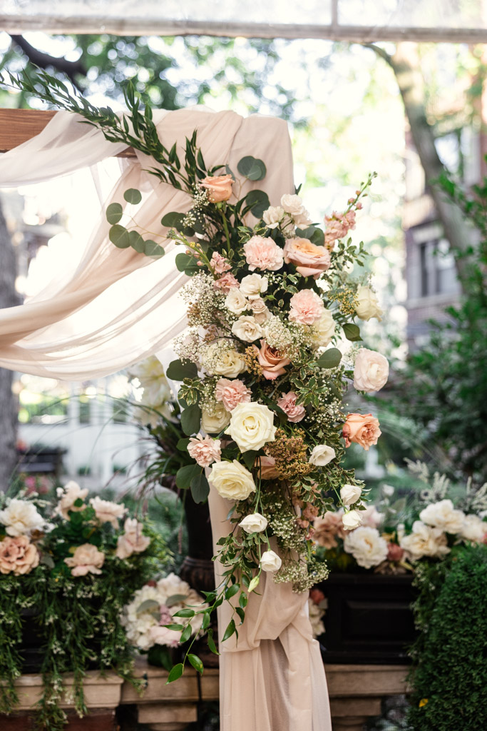 Wedding arch draped in beige fabric, adorned with white and blush flowers and lush greenery for Salvatore's wedding ceremony