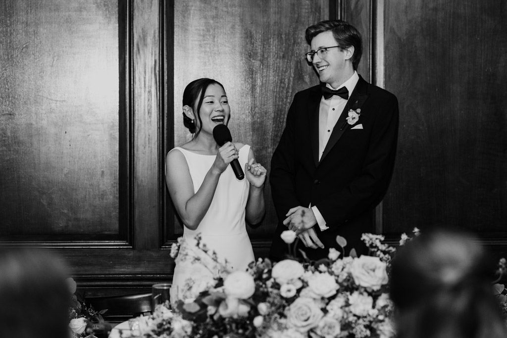Black and white photo of bride and groom speaking to their guests from the head table at their Salvatore's wedding reception