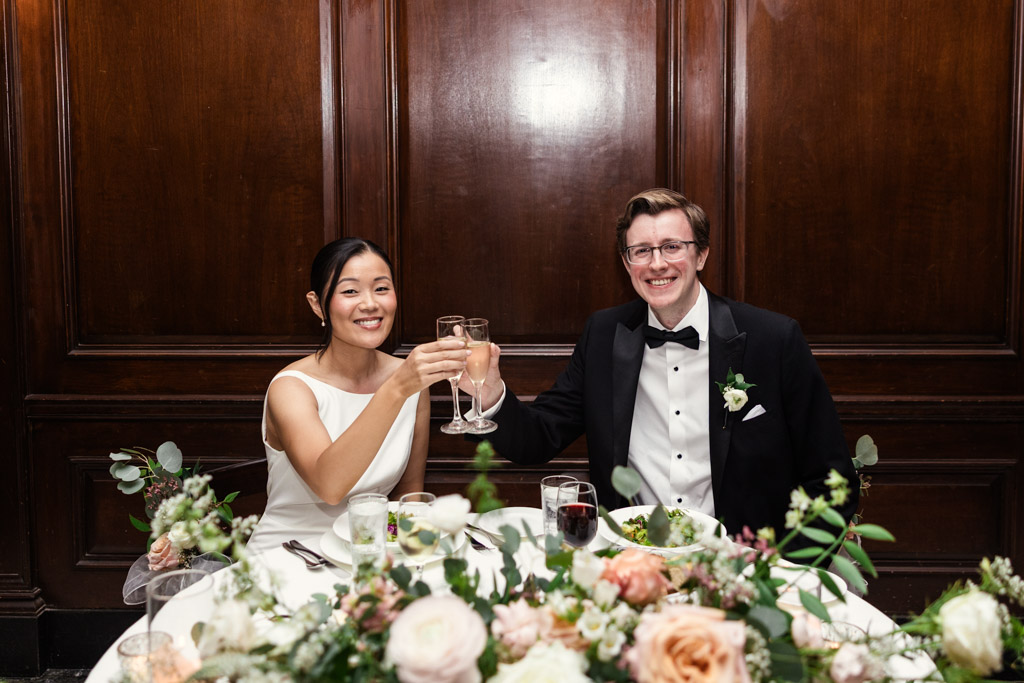 Bride and groom sit at a table, smiling and toasting with champagne during their wedding reception at Salvatore's