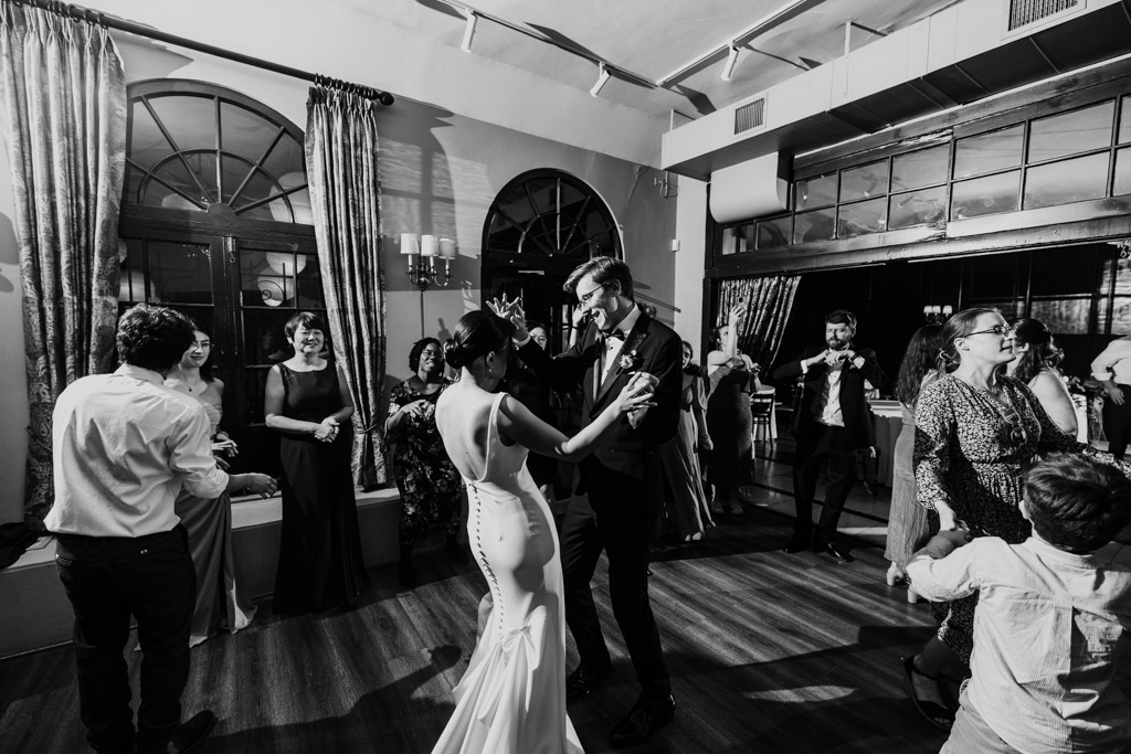 Black and white photo of bride and groom dancing together at their Salvatore's wedding reception, surrounded by celebrating guests