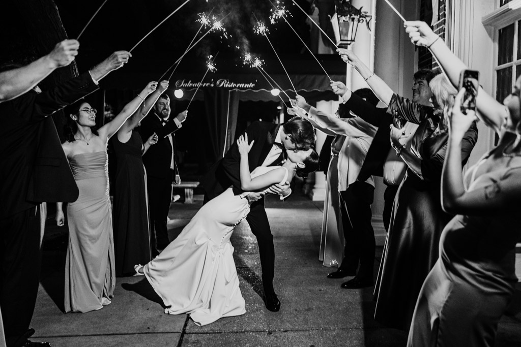 Black and white photo of newlyweds kissing as the groom dips the bride under sparklers held by guests during their Salvatore's wedding reception