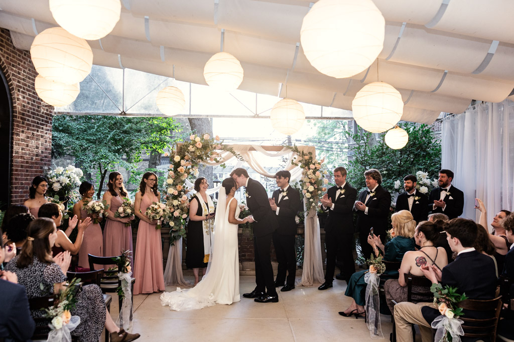 Bride and groom kiss, surrounded by their wedding party and guests at Salvatore's