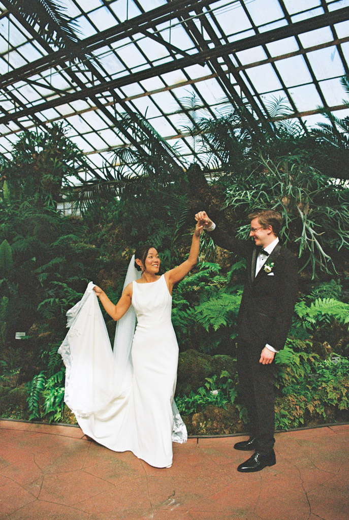 Film photo of bride and groom dancing together inside Lincoln Park Conservatory, surrounded by green plants under thge greenhouse's glass ceiling