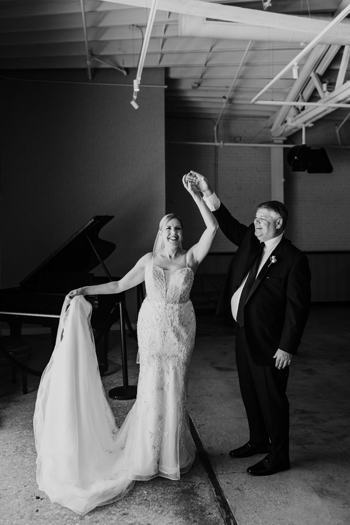 Black and white photo of bride and groom dancing together, smiling, with a piano in the background at their wedding celebration at Sarabande in Chicago