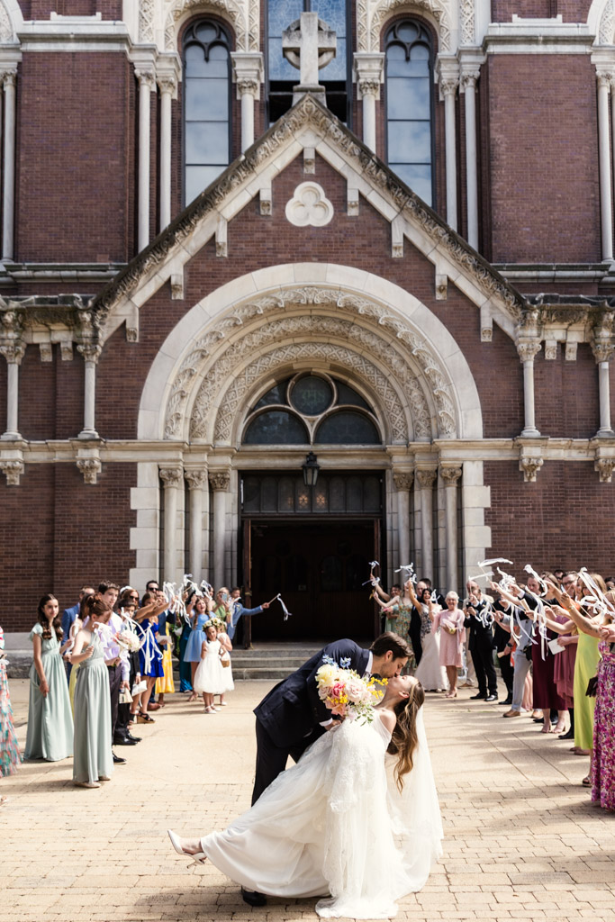 Bride and groom kiss outside a St. Michael's Church in Chicago's Old Town neighborhood as guests cheer and wave ribbons to celebrate their wedding