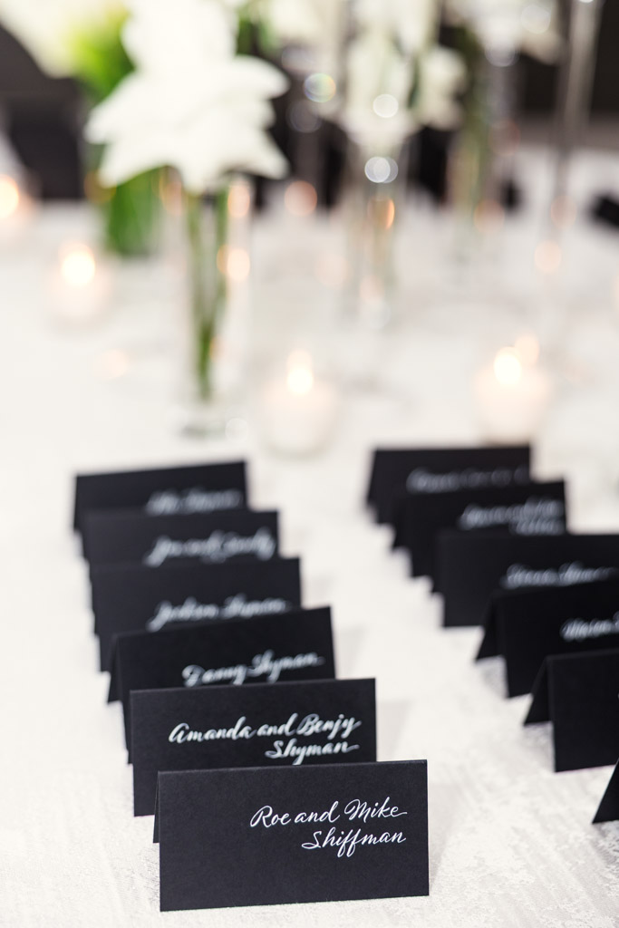 Black place cards with white script arranged on a table at The Four Seasons Chicago, with flowers and candles in the background