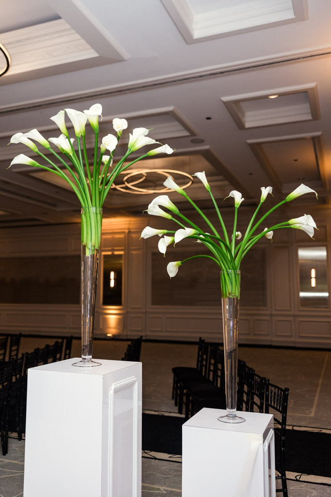 Two tall vases with white calla lilies on white pedestals in wedding reception space at The Four Seasons Chicago