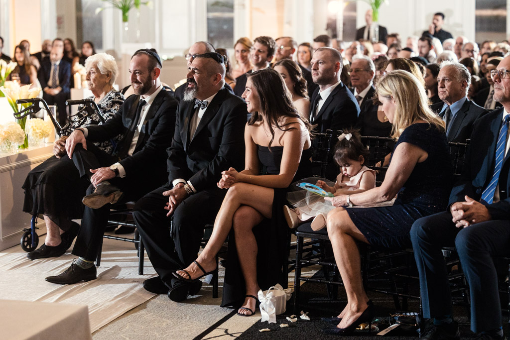 Wedding guests dressed formally sit and smile, watching the ceremony at The Four Seasons Chicago