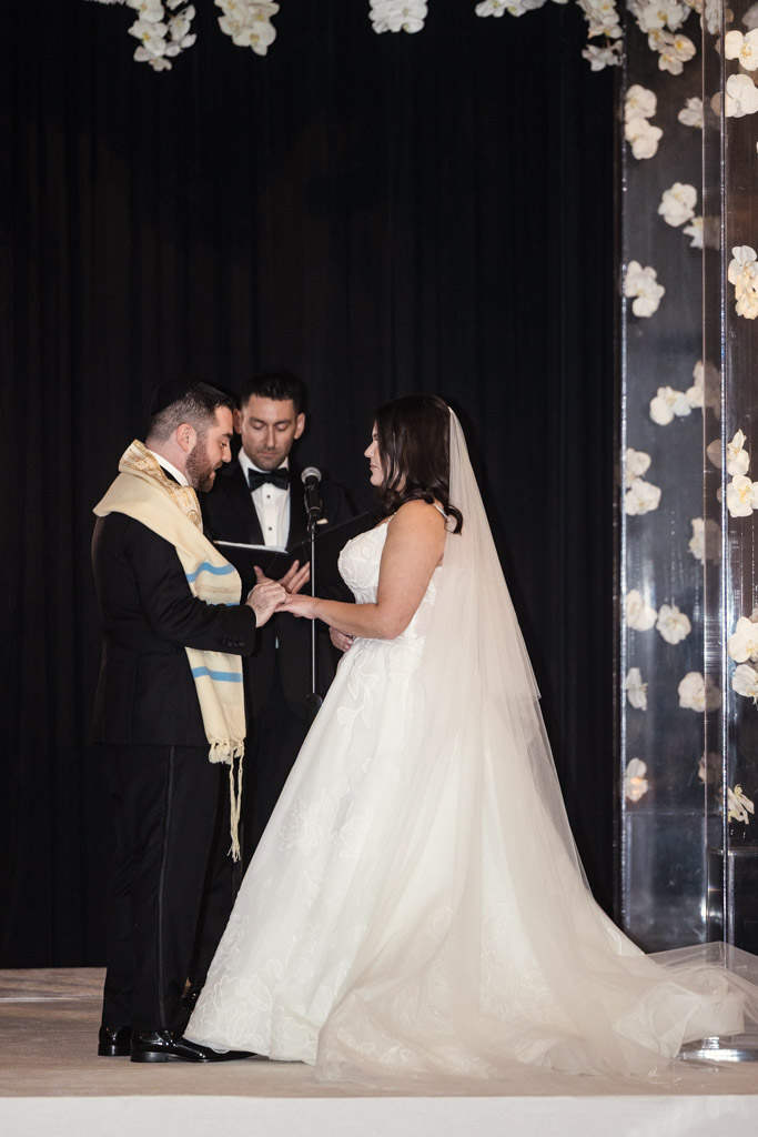 Groom places ring on bride's finger during their wedding ceremony with an officiant standing behind them at The Four Seasons Chicago