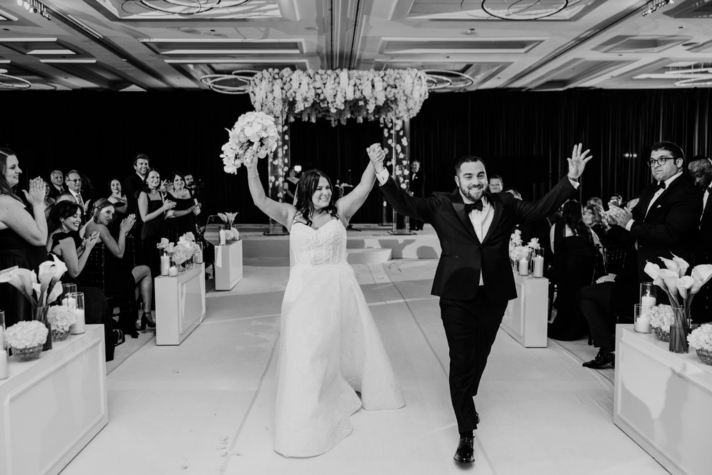 Black and white photo of bride and groom holding hands and smiling as they walk down the aisle after their Four Seasons Chicago wedding ceremony