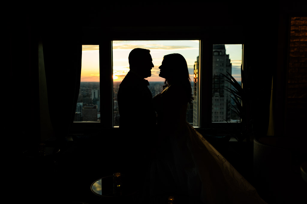 Silhouette of newlywed couple facing each other by a window at sunset with downtown buildings outside, at The Four Seasons Chicago