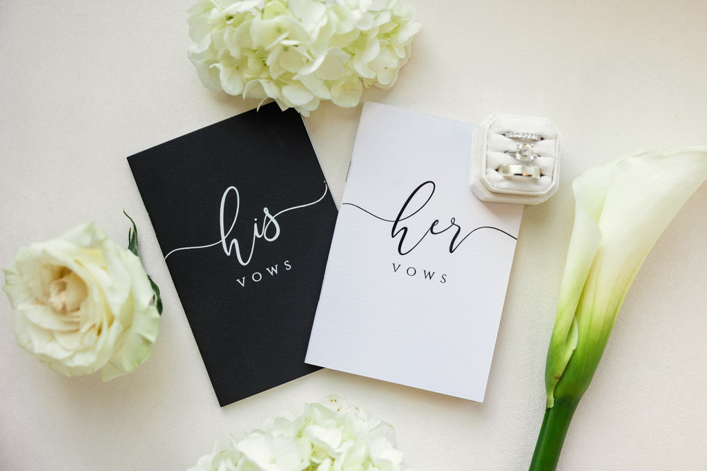 His and her vow books with flowers, a calla lily, and a ring box with wedding rings displayed on a white surface at The Four Seasons Chicago