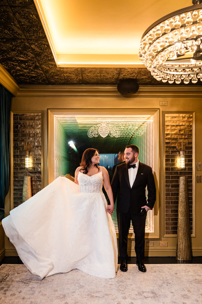 Bride in a white gown and groom in a black tuxedo smile at each other in an elegant, gold-lit room at The Four Seasons Chicago.