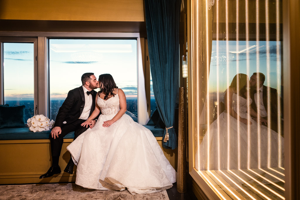 Bride and groom kiss on a window seat at sunset at The Four Seasons Chicago, with their reflection visible in a nearby mirror