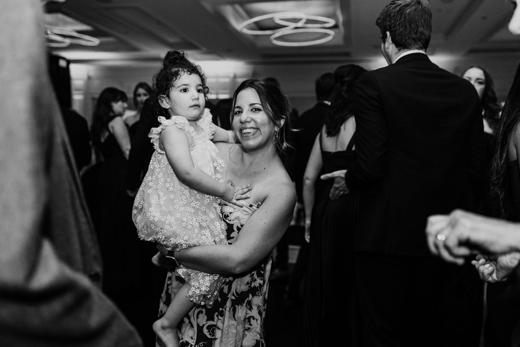 Woman smiling and holding a young girl in a dress at The Four Seasons Chicago wedding reception, with people dancing in the background
