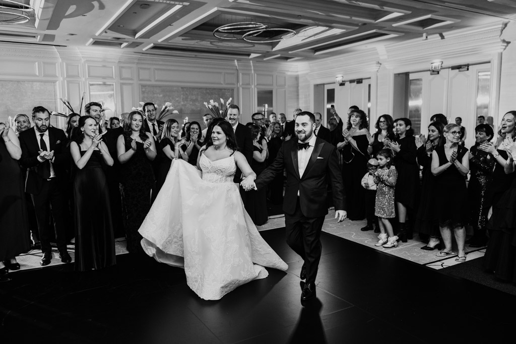 Black and white photo of bride and groom walking hand in hand as guests applaud at their The Four Seasons Chicago wedding reception