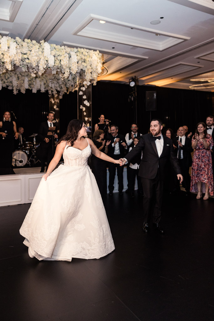 A bride and groom dance at their wedding reception at The Four Seasons Chicago, surrounded by smiling guests and a band