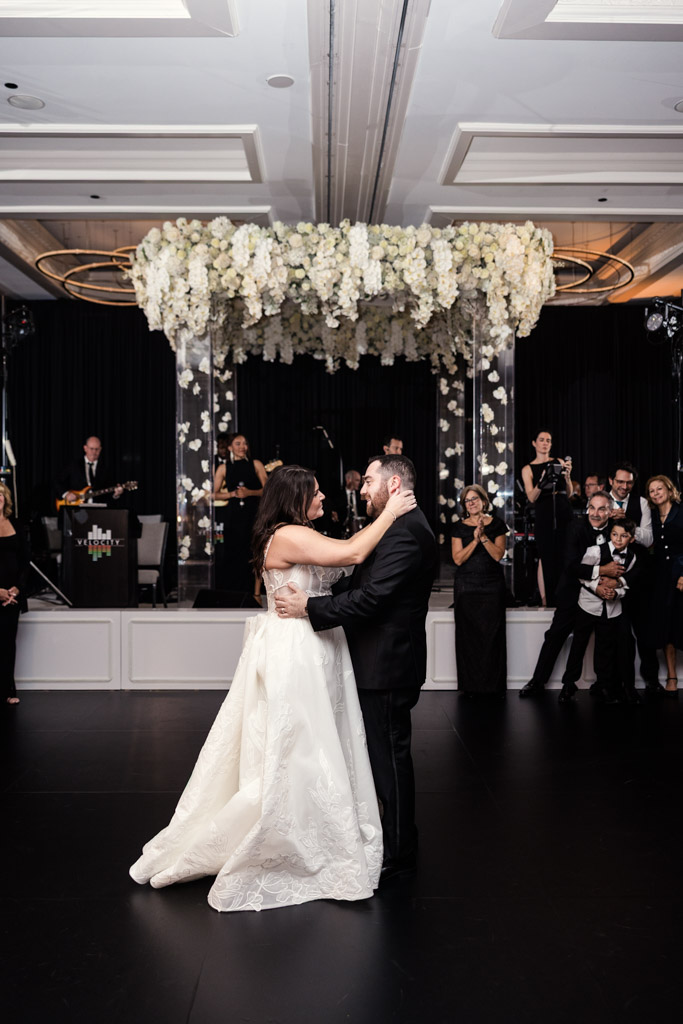 Bride and groom share their first dance in a ballroom of The Four Seasons Chicago as guests watch and smile