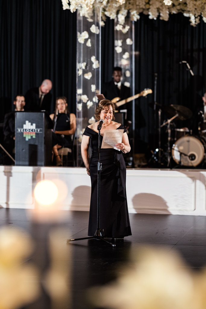 A woman in a black dress gives a speech with a band behind her during wedding reception at The Four Seasons Chicago