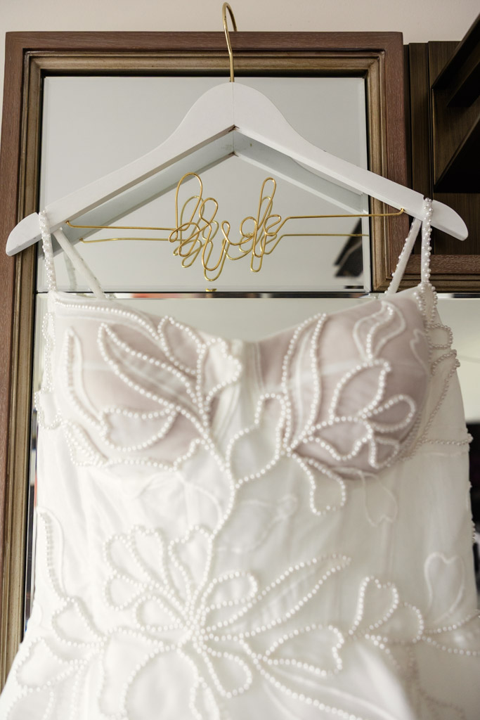 A white wedding dress with pearl details hangs on a hanger that says 