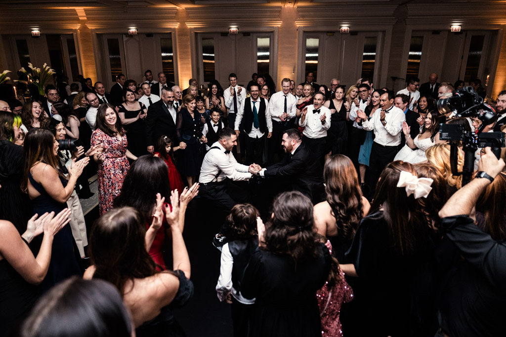 Groom and friend dance together, surrounded by cheering guests in formal attire at wedding reception at The Four Seasons Chicago