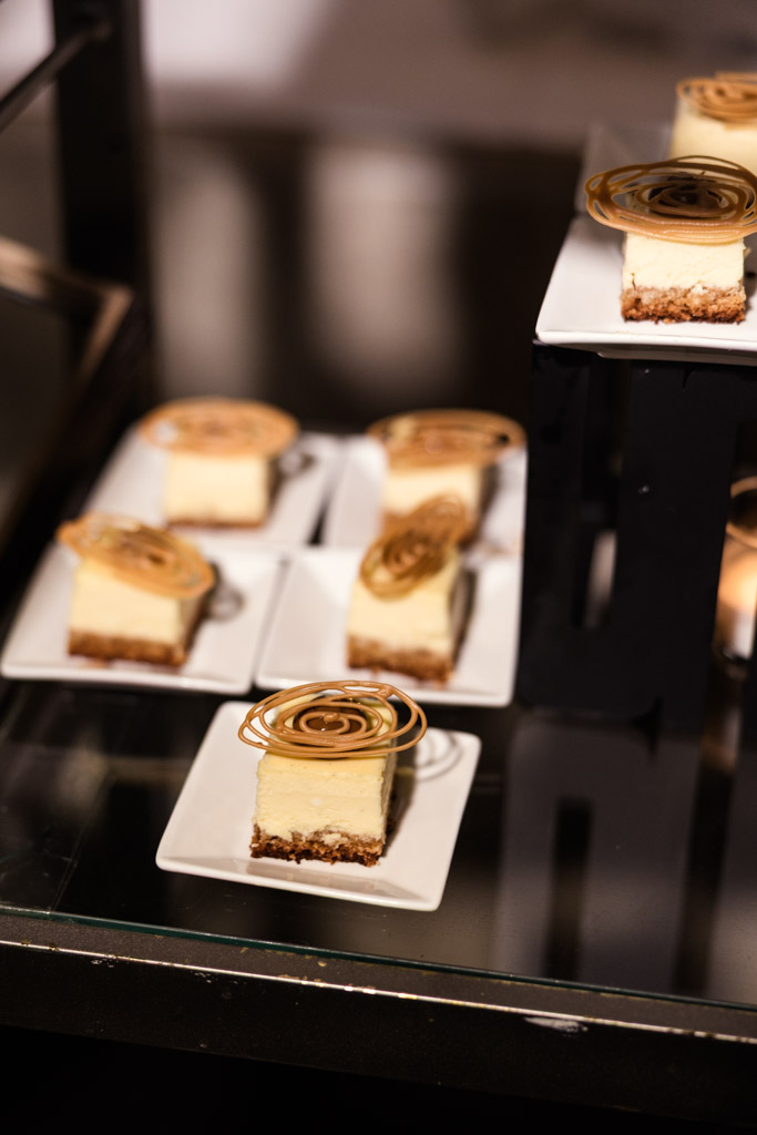 Several small cheesecake slices with caramel swirls on square white plates, displayed on a glass shelf for wedding reception at The Four Seasons Chicago