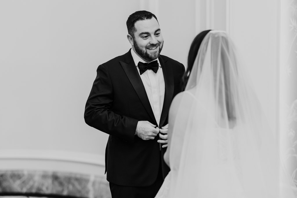 Black and white photo of groom in a suit smiling at a bride in a veil during their first look at The Four Seasons Chicago