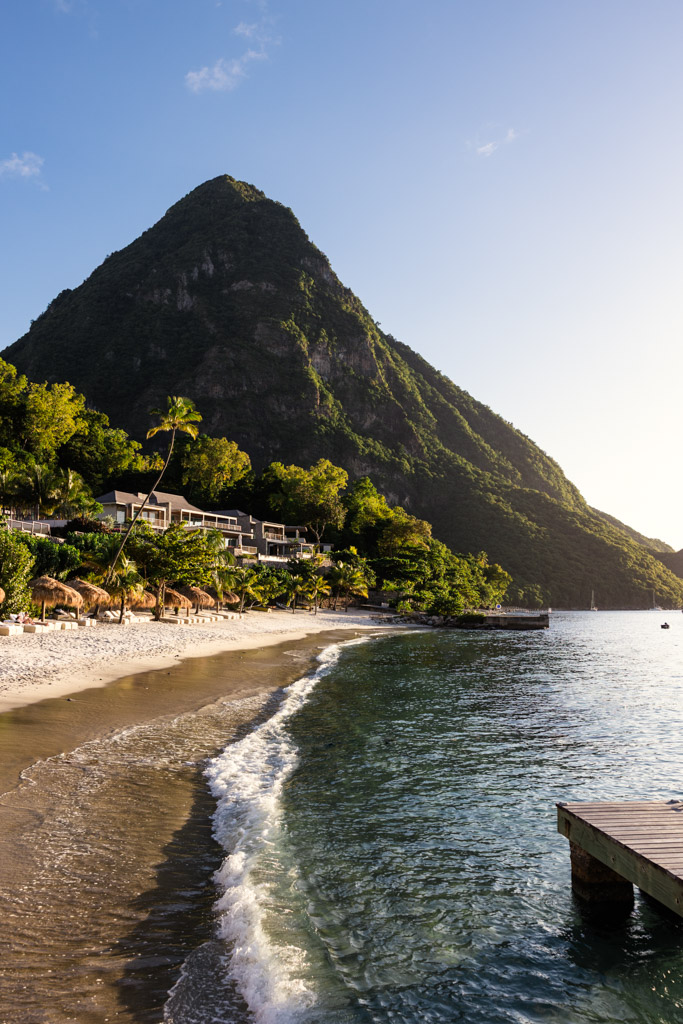 A sandy beach at Viceroy Sugar Beach resort in St. Lucia with gentle waves, lush greenery, and Gros Piton