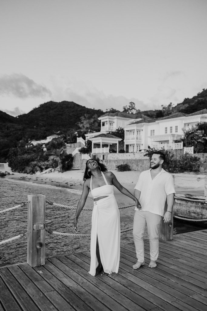 Black and white photo of woman laughing with her partner on a dock by the water at Viceroy Sugar Beach