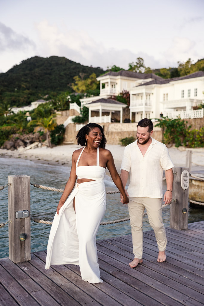 Newlyweds holding hands and smiling on a wooden dock by the water at Viceroy Sugar Beach in St. Lucia