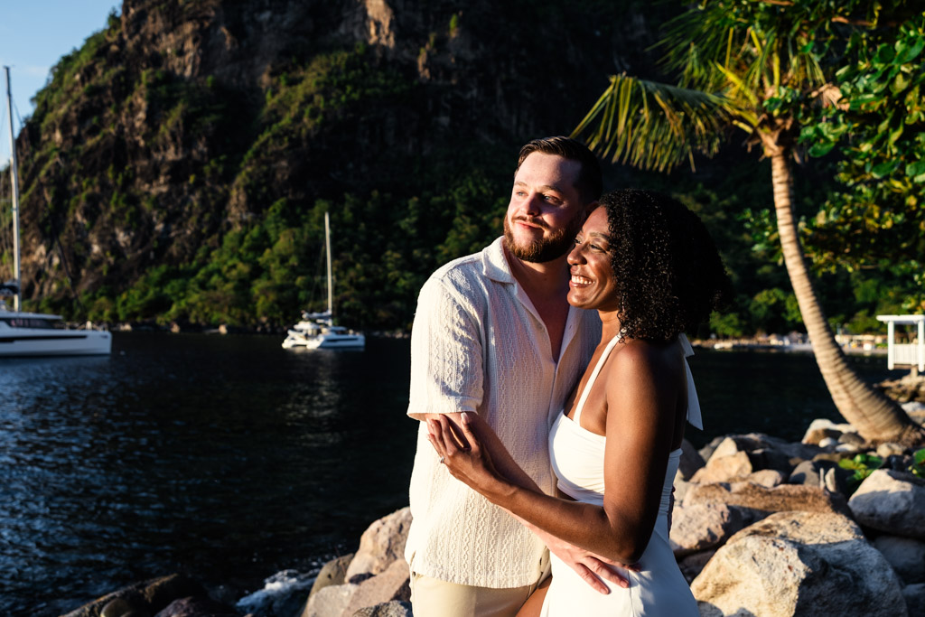 Happy newlywed couple by the water at sunset with boats and Petit Piton in the background at Viceroy Sugar Beach in St. Lucia