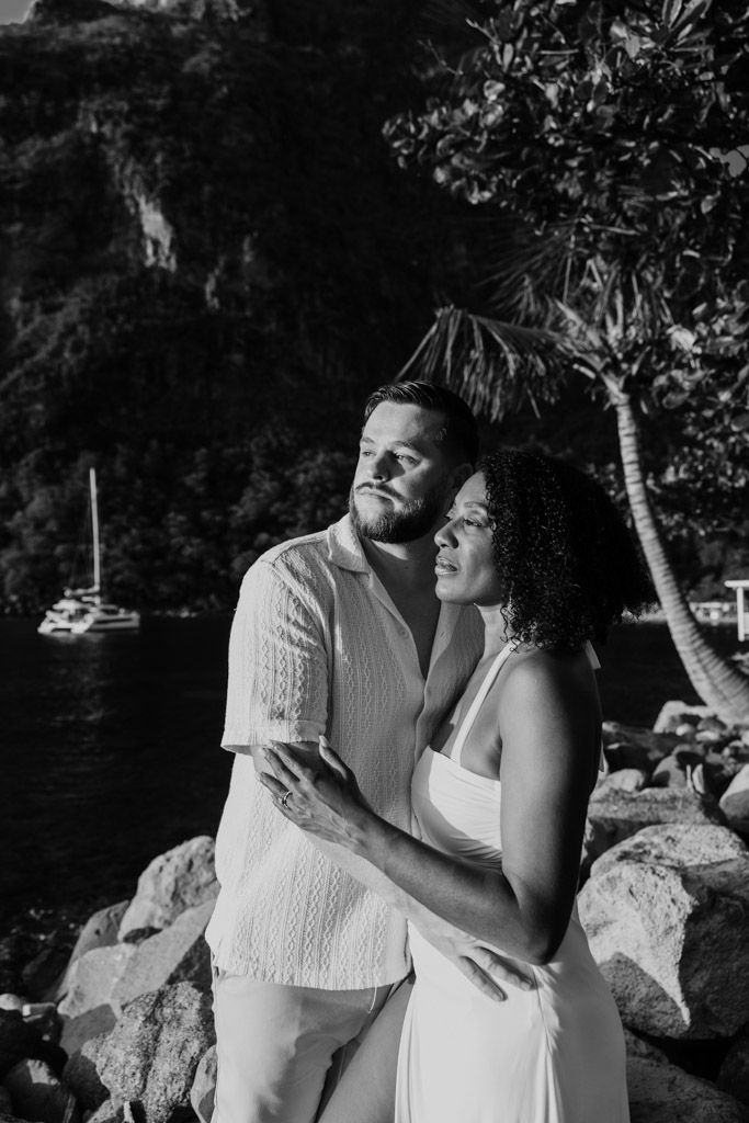 Black and white photo of couple embracing on the rocky shore at Viceroy Sugar Beach, gazing into the distance