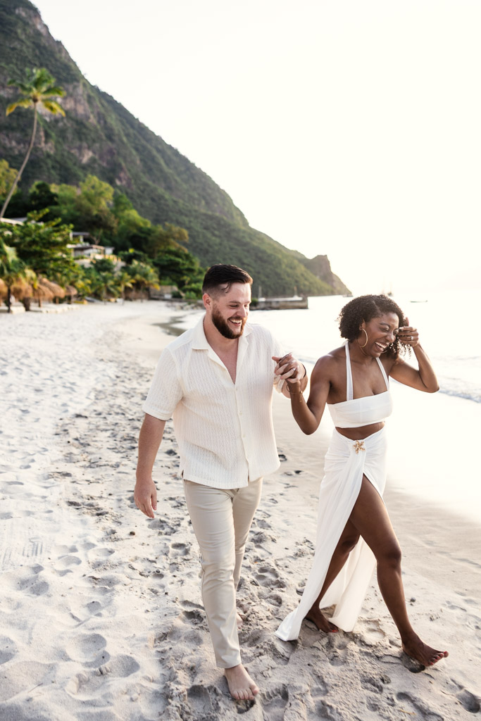 Smiling newlywed couple holding hands and walking barefoot on a sandy beach on St. Lucia