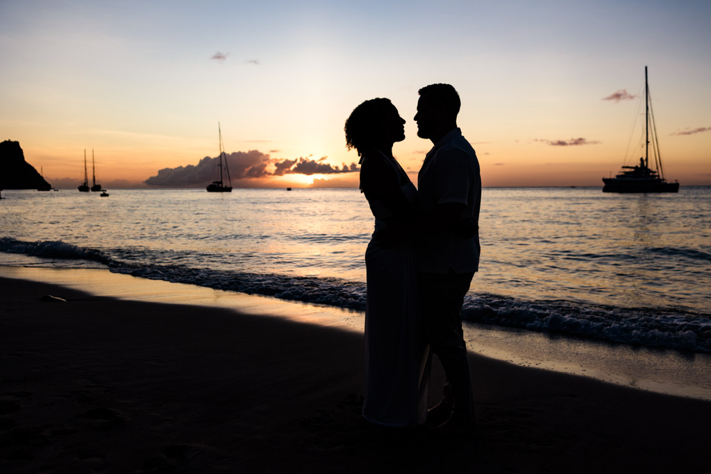 Silhouetted couple embracing on a beach at sunset with sailboats on the water in the background at Viceroy Sugar Beach