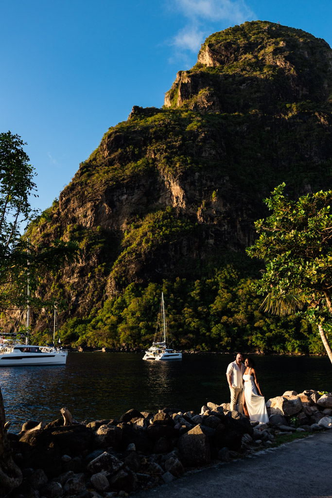 Newlywed couple poses by the water at Viceroy Sugar Beach, with sailboats and Petit Piton in the background at sunset