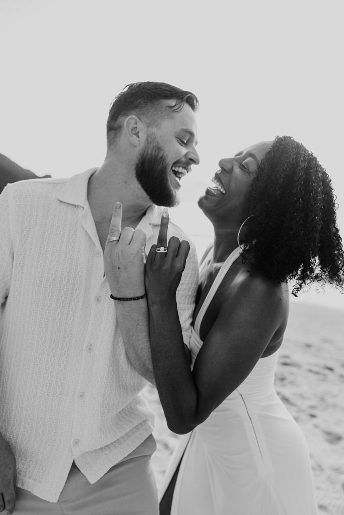 Black and white photo of newlywed couple laughing on the beach at Viceroy Sugar Beach, showing off their wedding rings