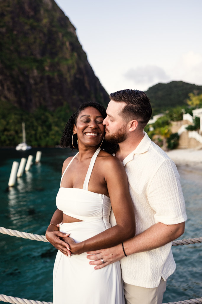 Newlyweds embrace and smile by the ocean at Viceroy Sugar Beach, with Petit Piton in the background
