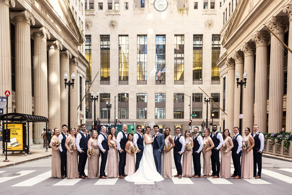 The Wildman BT wedding party poses in formal attire on a city street, with tall buildings and the 