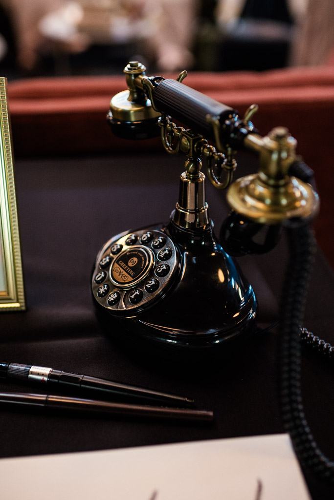 A vintage black rotary telephone sits on a dark desk beside a pen and a picture frame from the Wildman BT wedding.