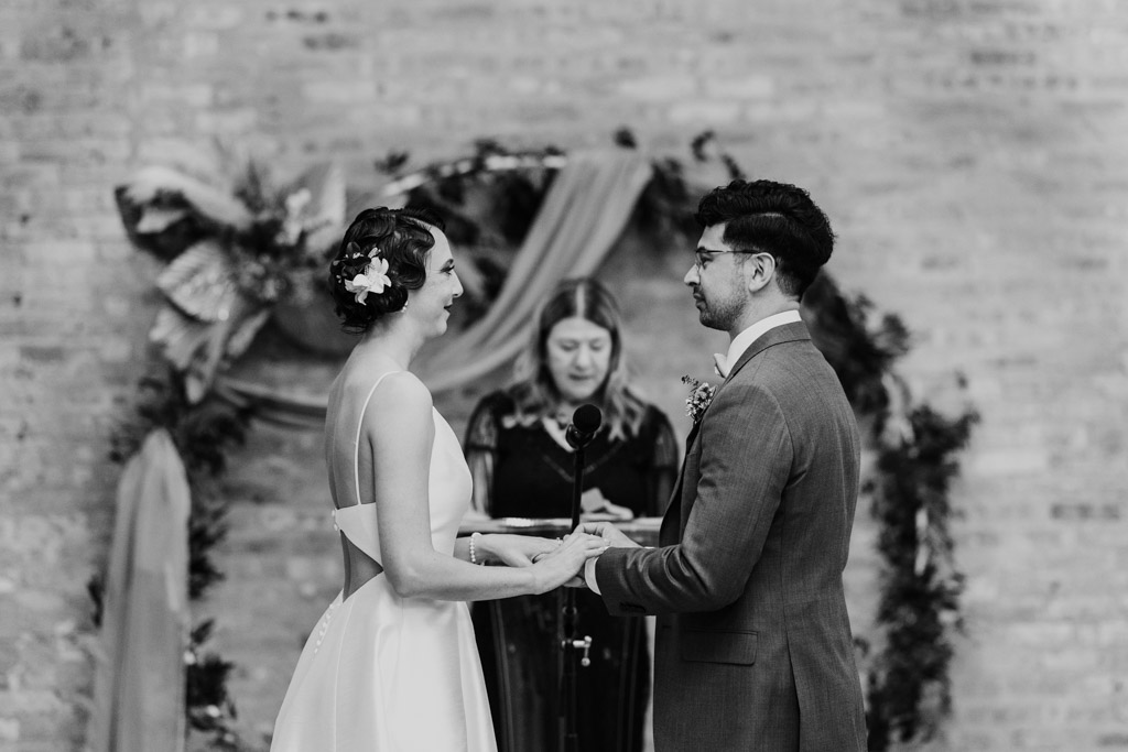 A bride and groom stand holding hands during their Wildman BT wedding ceremony, officiant in the background.