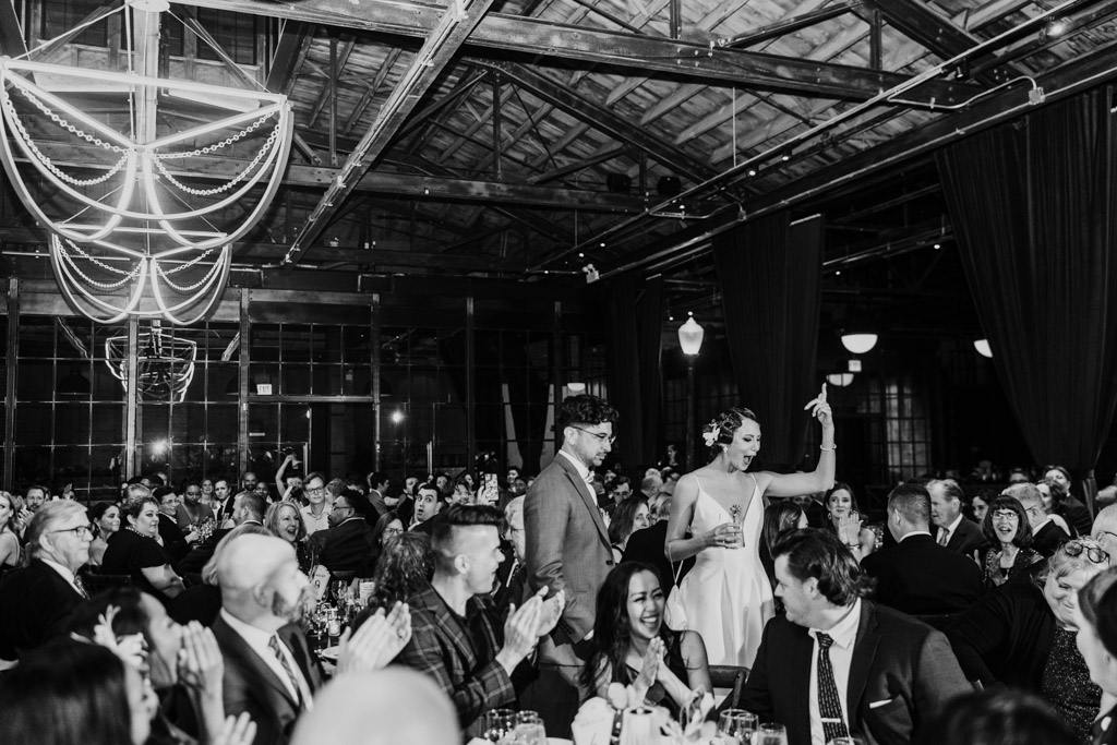 A bride and groom walk through a cheering crowd at a festive indoor reception, celebrating their unforgettable Wildman BT wedding.