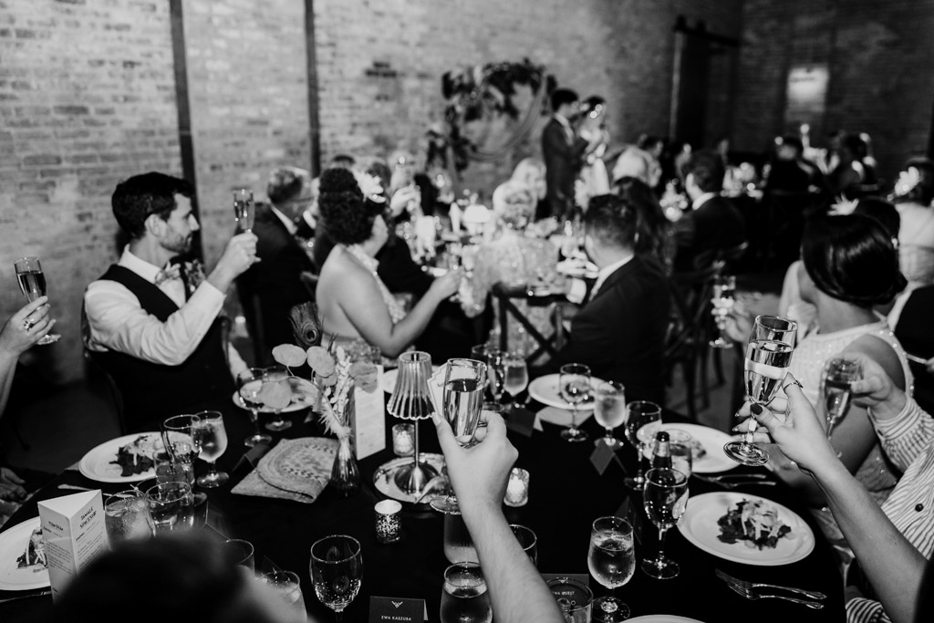 People at a formal dinner raising glasses for a toast, with the couple, celebrating their Wildman BT wedding, standing at the front of the room.